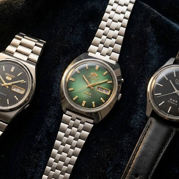 Three vintage watches with different colored faces on a dark fabric background